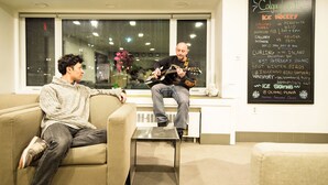 Dos personas sentadas en un sofá en una habitación con una ventana y una pared mostrando información de eventos.