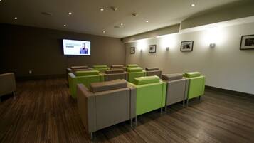 A conference room with rows of chairs, a projection screen, and framed pictures on the wall.