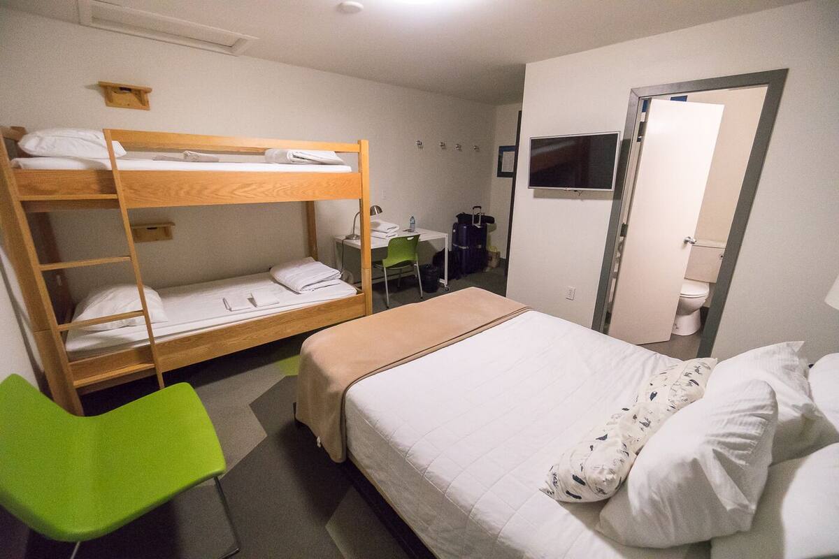 A room with a bunk bed, a single bed, a desk with a chair, a mirror, and a television.