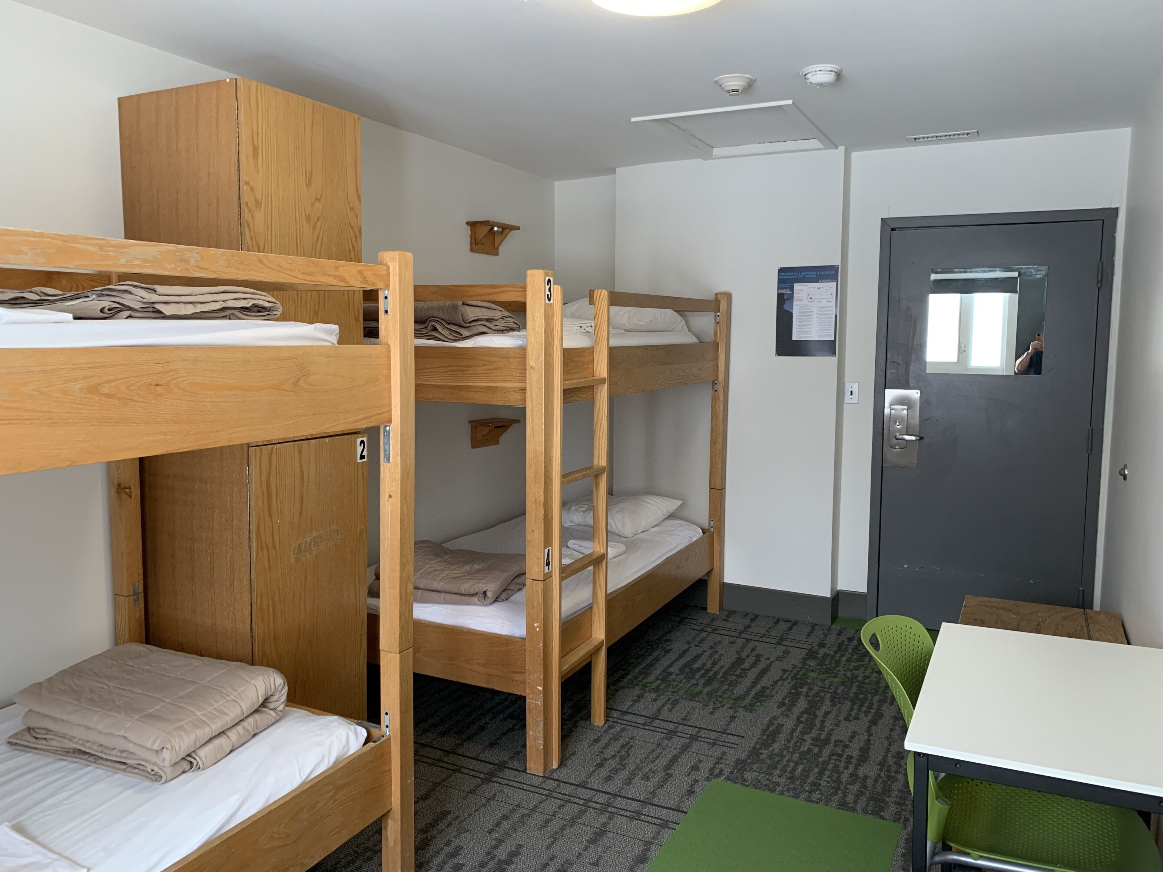 A dormitory room with bunk beds, a desk, a chair, and a door.