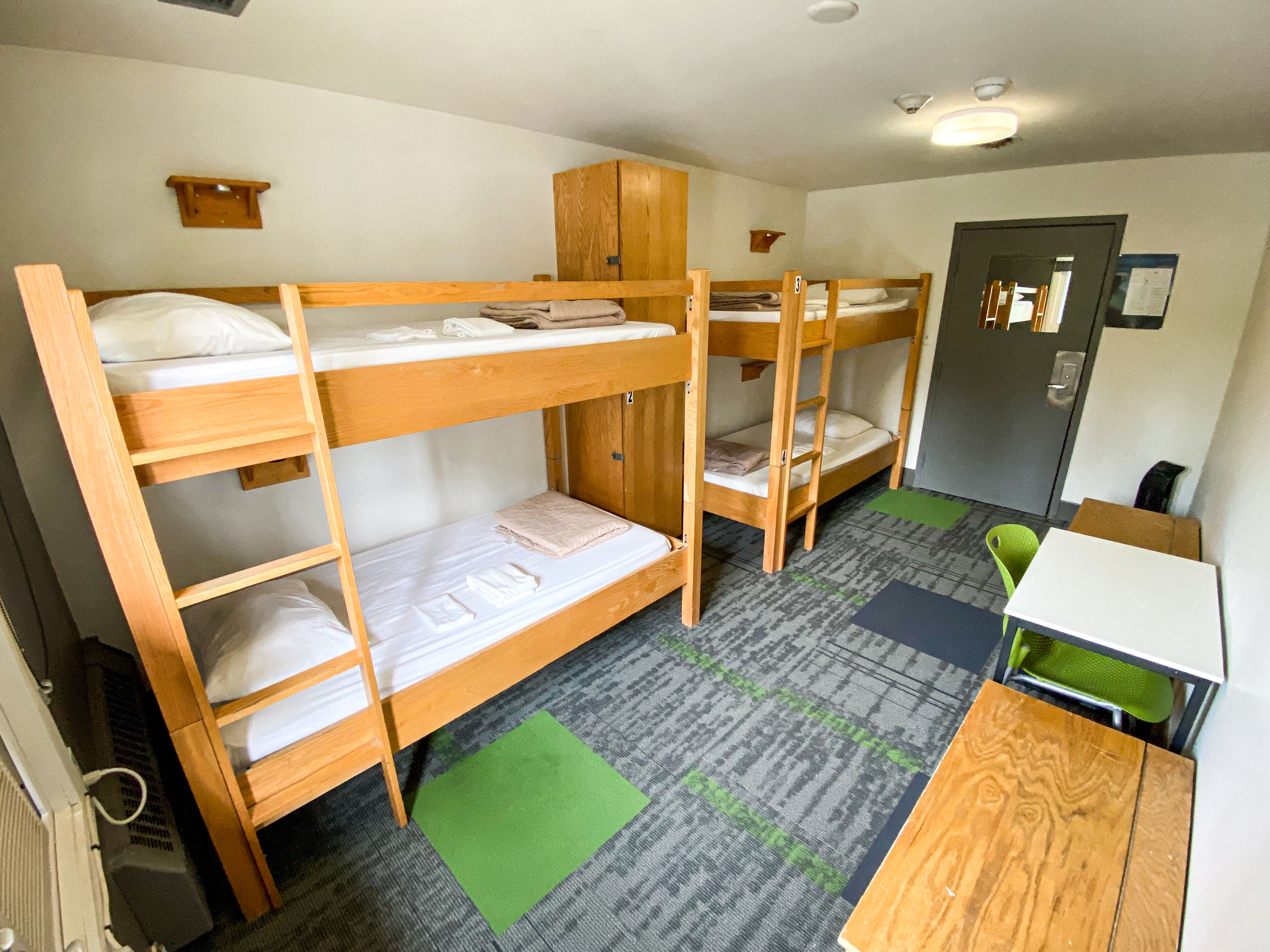 A dormitory room with bunk beds, a desk, a chair, and a cabinet.