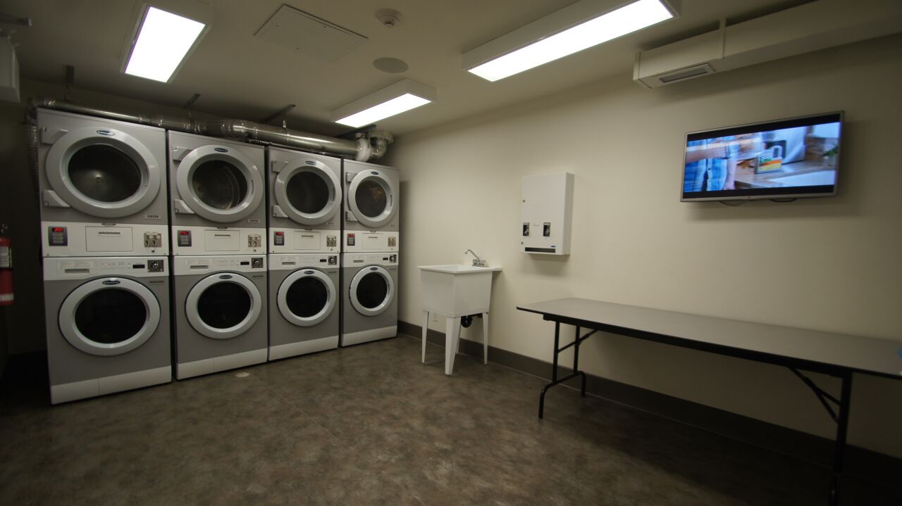 Een wasserette met meerdere wasmachines, een wasbak en een televisie aan de muur.