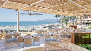 An outdoor dining area with tables and chairs, overlooking a beach and the sea. - Villa del Palmar Flamingos Beach Resort & Spa (Nuevo Nayarit)