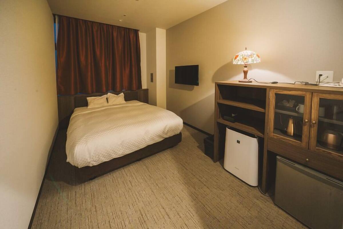 Une chambre d’hôtel équipée d’un lit, d’une télévision, d’une lampe, d’un mini-réfrigérateur et d’un placard.