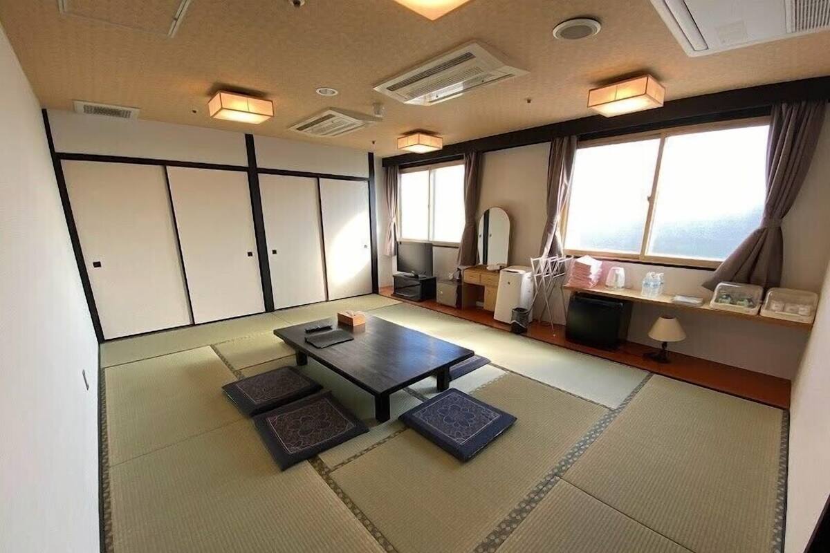 Une pièce de style japonais traditionnel, avec un sol recouvert de tatamis, une table basse, un canapé et une fenêtre avec des rideaux.