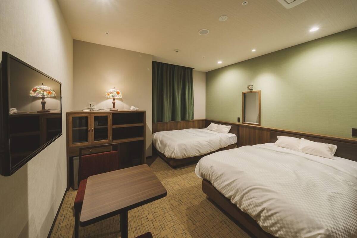 Une chambre d’hôtel avec deux lits, un bureau, une chaise, une petite table, un miroir et une armoire.