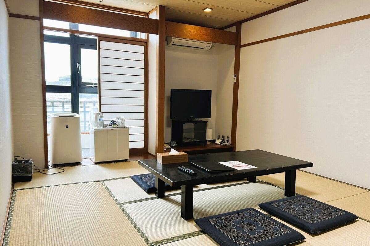 Une pièce avec un sol recouvert de tatamis, une table noire avec une télécommande, un téléviseur et un climatiseur blanc.