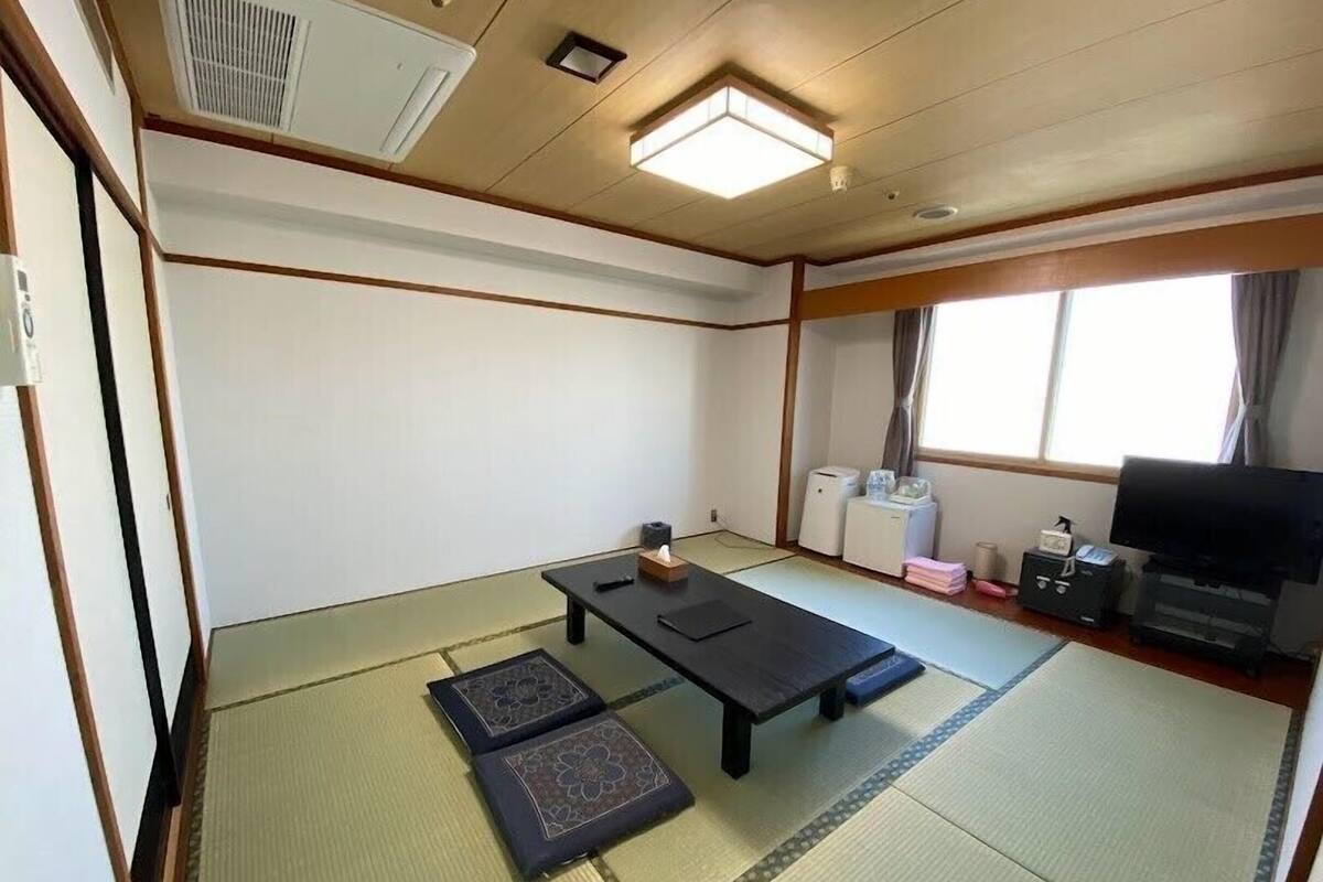 Une pièce avec un sol recouvert de tatamis, une table en tatami, une télévision et un radiateur.