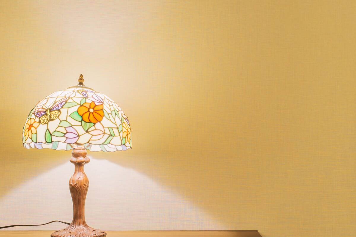 Une lampe de table avec un abat-jour en vitrail, posée sur une table en bois devant un mur uni.