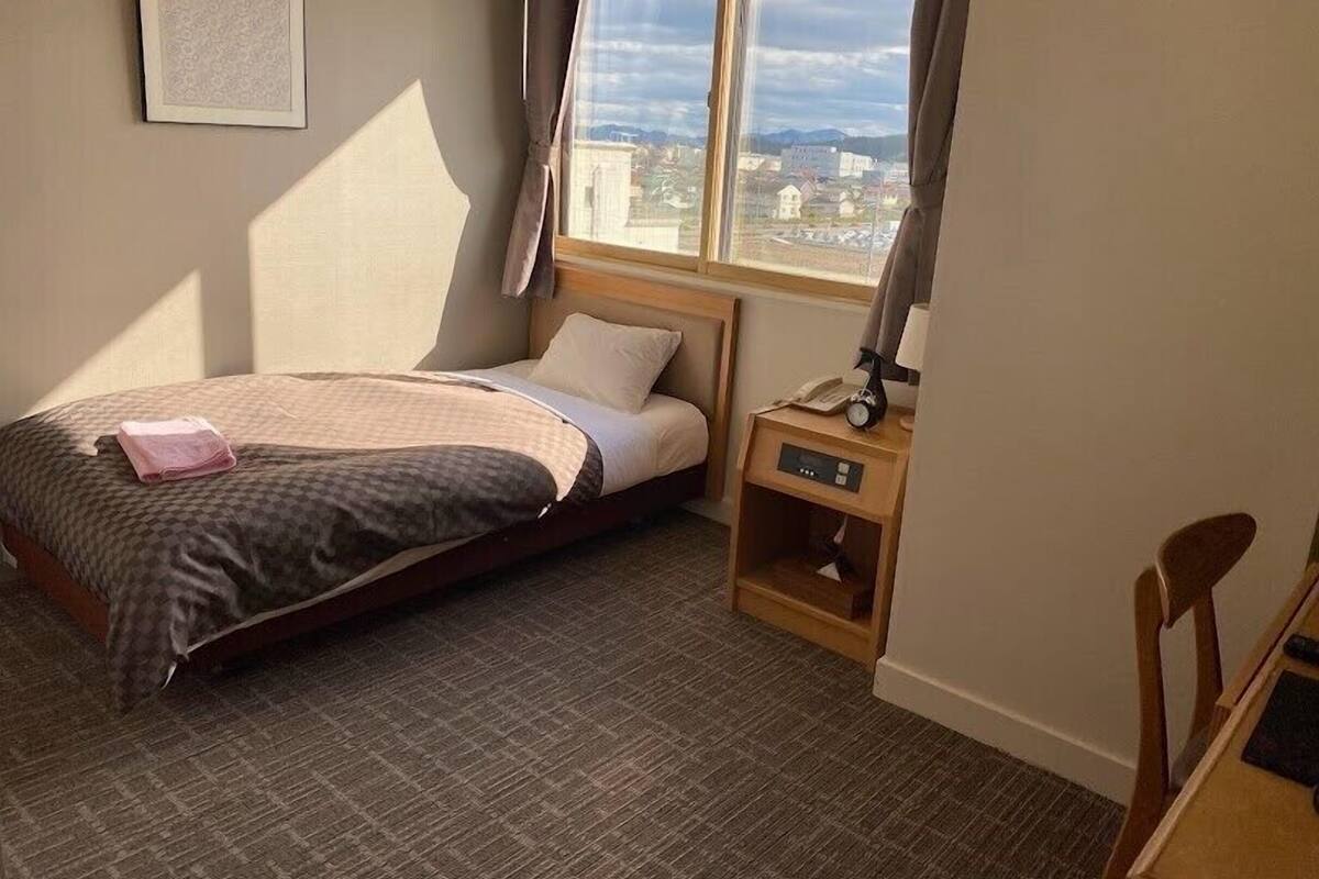 Une chambre à coucher comprenant un lit, une table de chevet, une chaise, une fenêtre donnant sur un beau paysage et un tableau accroché au mur.