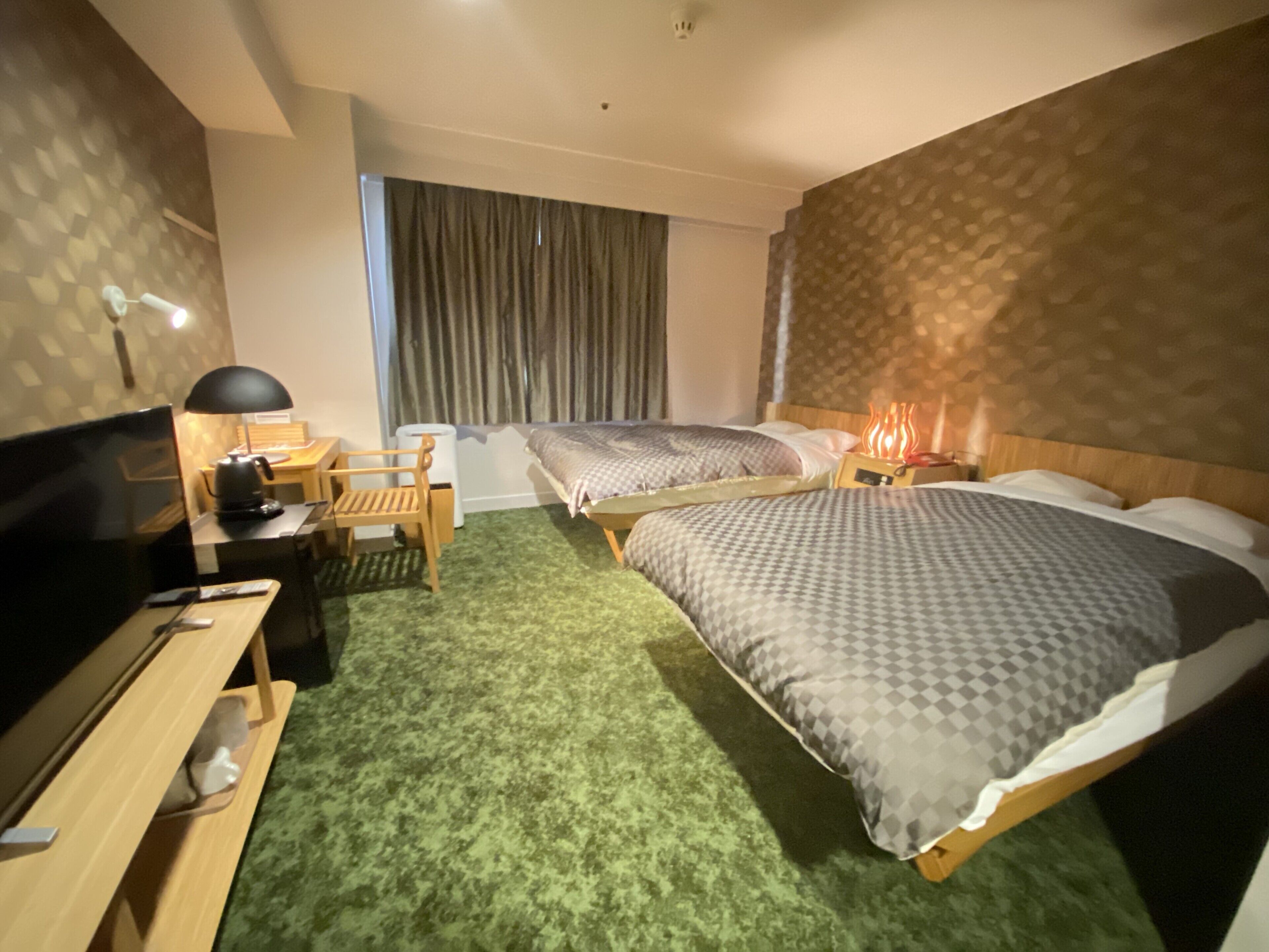 A hotel room with two beds, a desk with a lamp, a TV, and a window with curtains.
