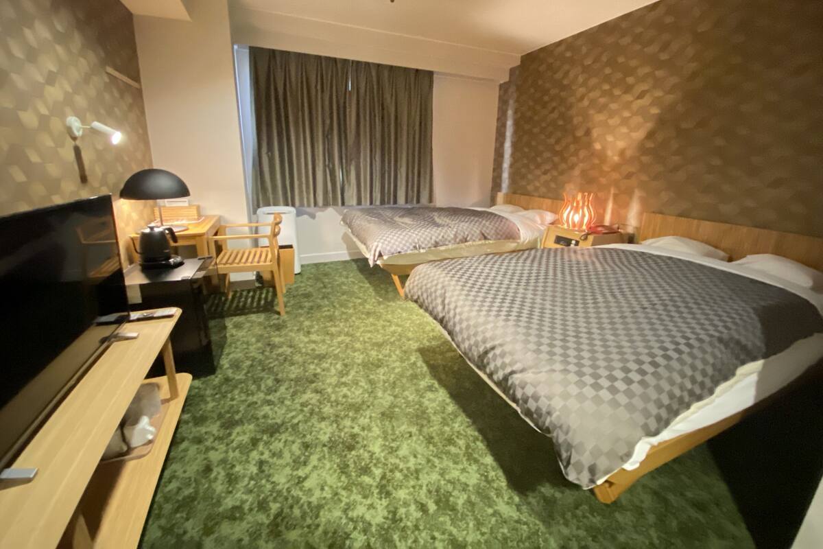 Une chambre d’hôtel avec deux lits, un bureau avec une lampe, une télévision et une fenêtre avec des rideaux.