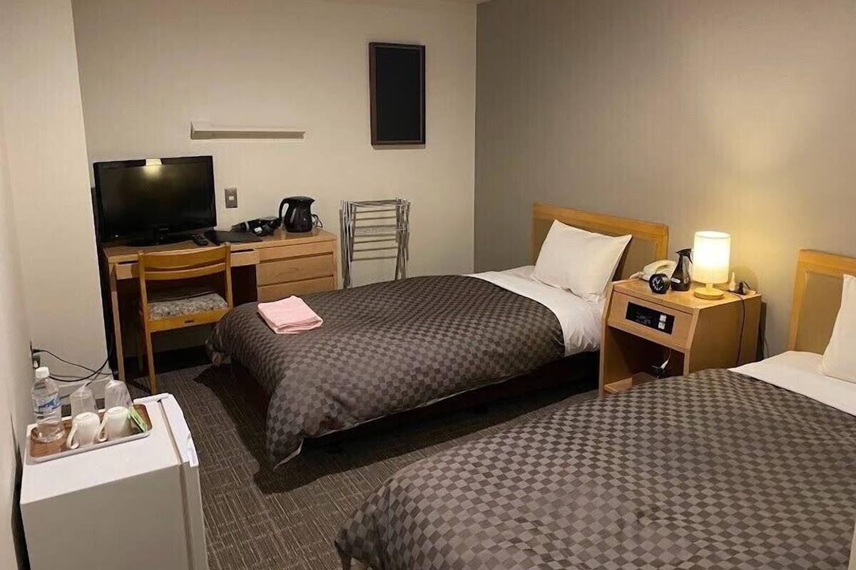 Une chambre d’hôtel avec deux lits, un bureau avec une télévision, une machine à café et une table de chevet avec une lampe.