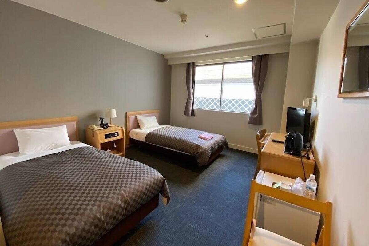 Une chambre d’hôtel avec deux lits, un bureau avec une chaise, une télévision et une fenêtre avec des rideaux.