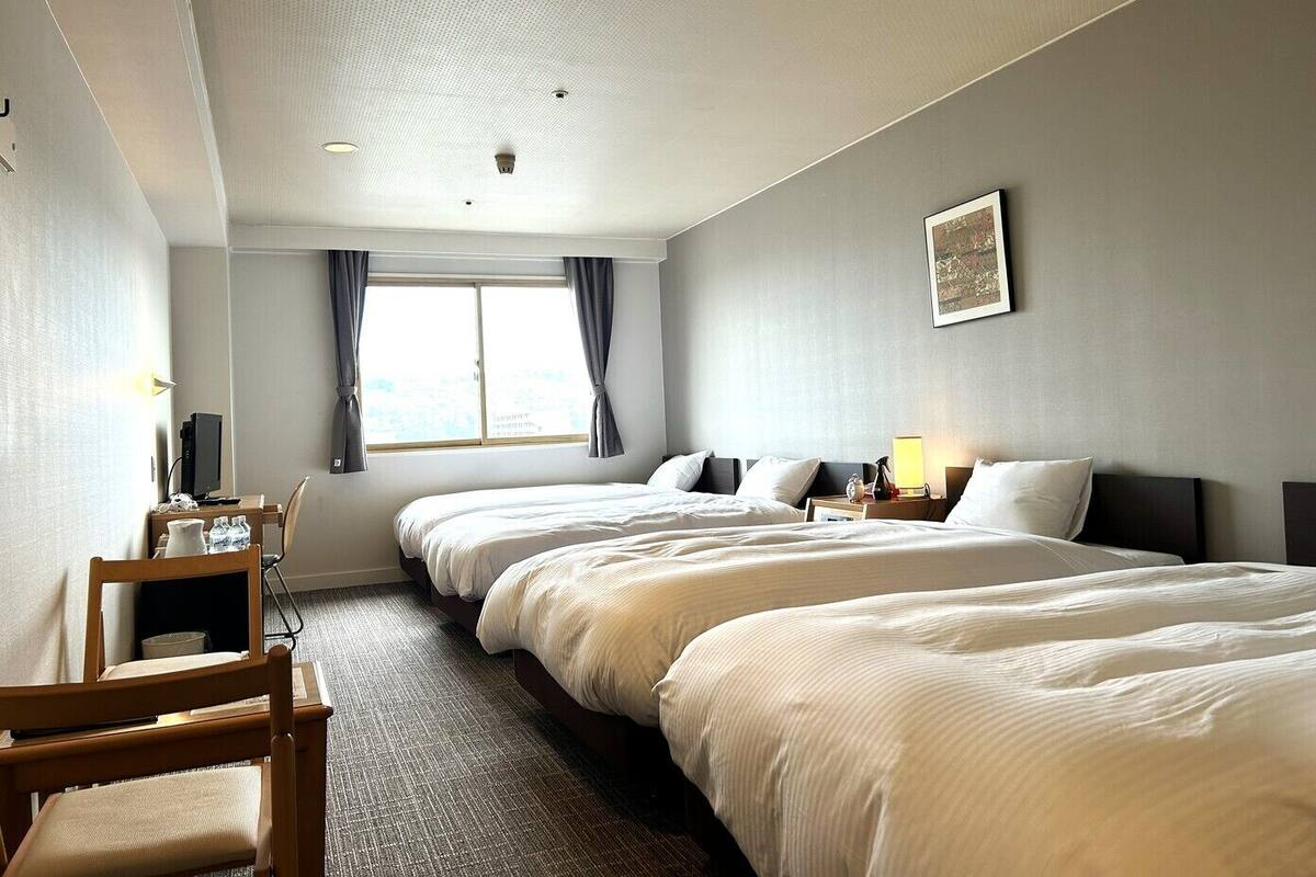 Une chambre d’hôtel avec deux lits, un bureau, une chaise, une fenêtre avec des rideaux et un tableau au mur.