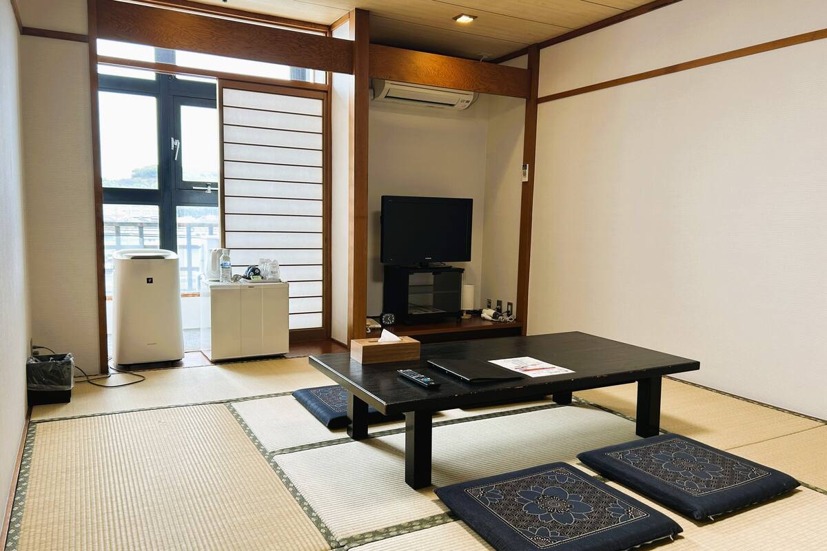 Une pièce de style japonais traditionnel, avec un sol recouvert de tatamis, une table basse, un téléviseur et un radiateur.