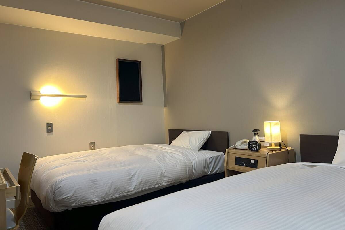 Une chambre d’hôtel avec deux lits, une table de chevet avec une lampe, un téléphone et un luminaire fixé au mur.