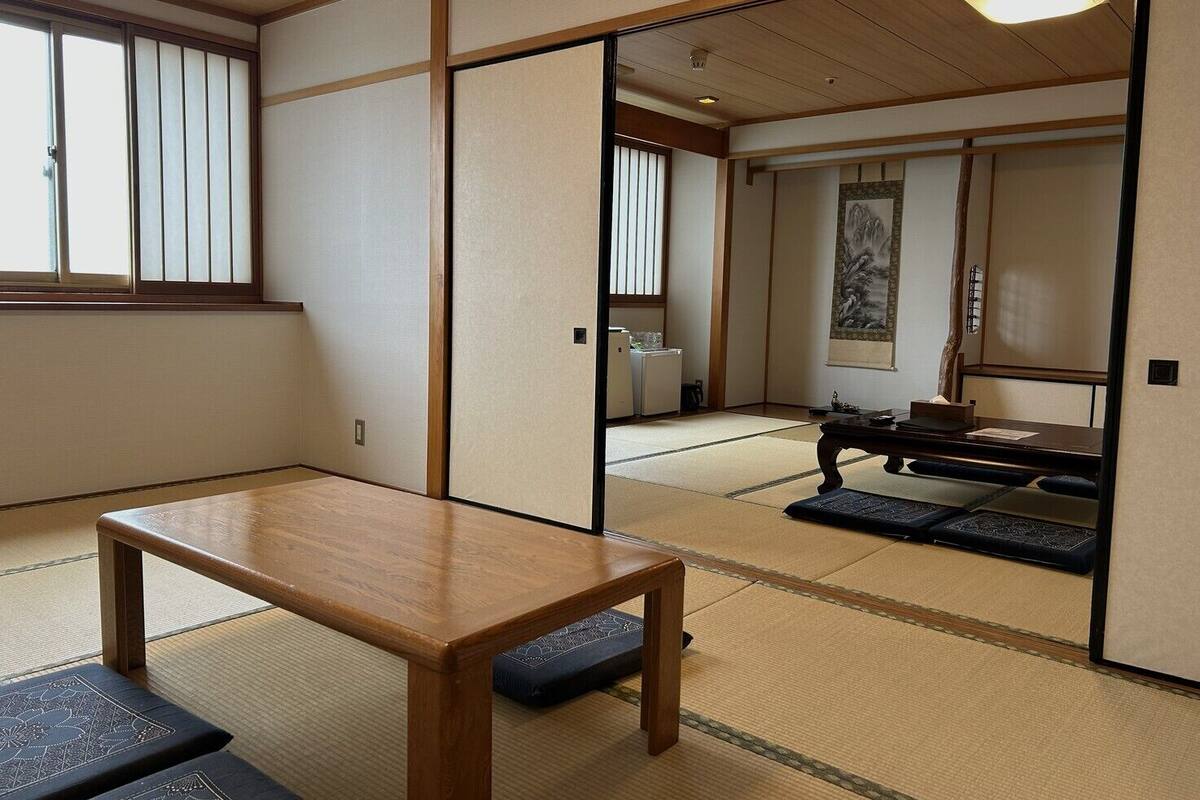 Une pièce de style japonais traditionnel, avec un sol recouvert de tatamis, une basse table en bois, des portes coulissantes et une vue sur un jardin japonais traditionnel.