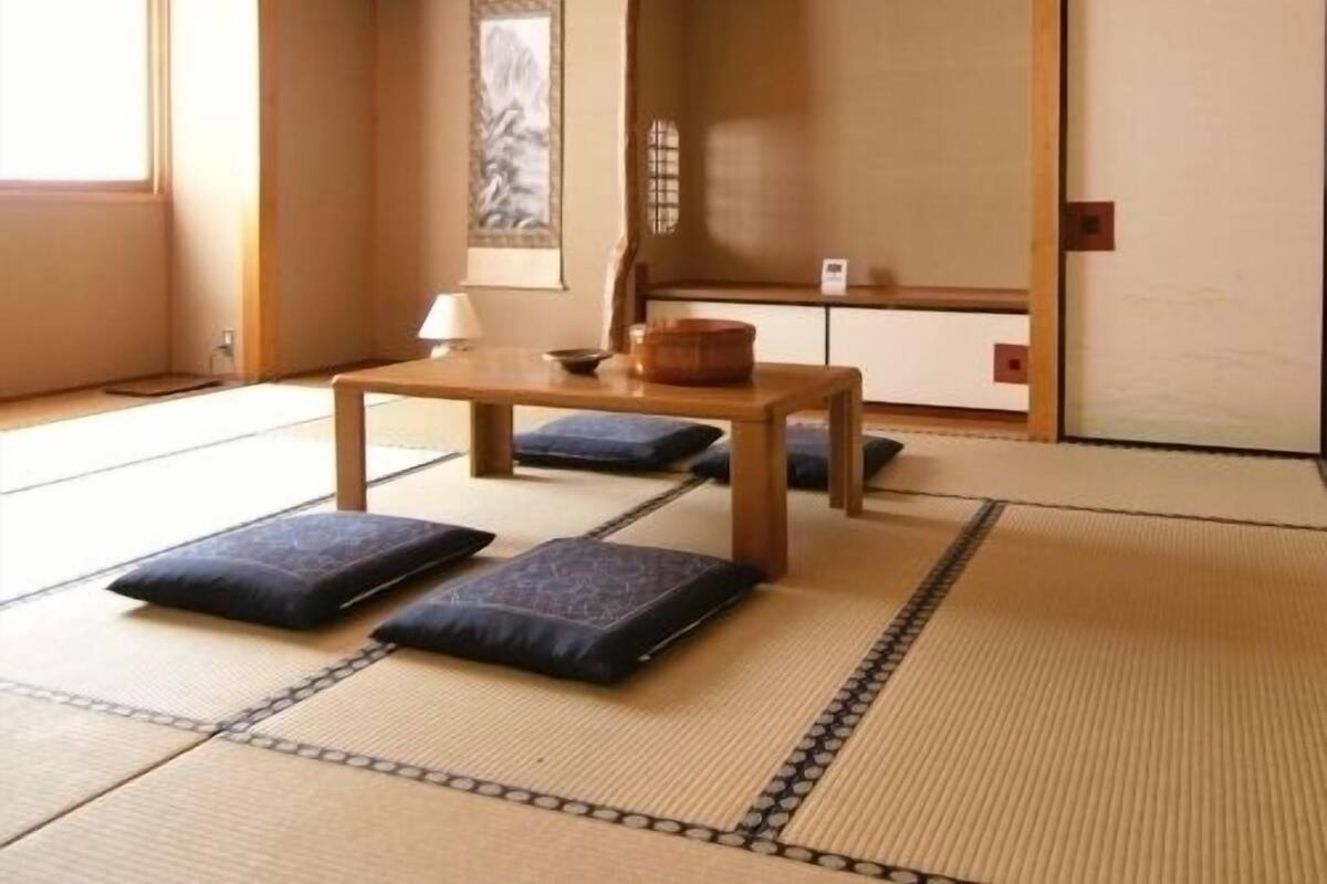 Une pièce avec un sol recouvert de tatamis, une petite table basse, des coussins et une porte coulissante.