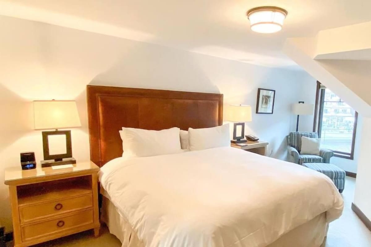 A hotel room with a large bed, bedside tables, a chair, and a window.