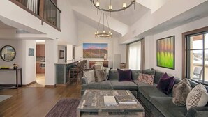 A spacious living area with a large sectional sofa, a wooden coffee table, and a view of the city through large windows.