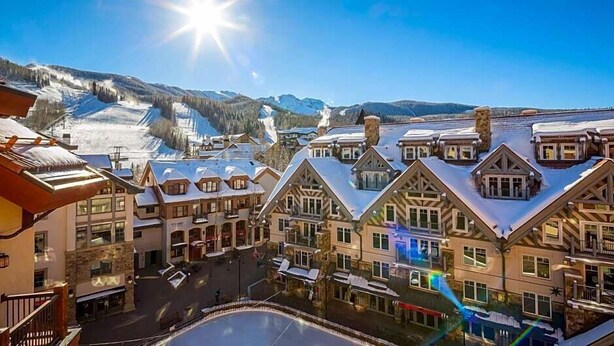 A ski resort with traditional chalet-style buildings, a central square, and a mountain backdrop.