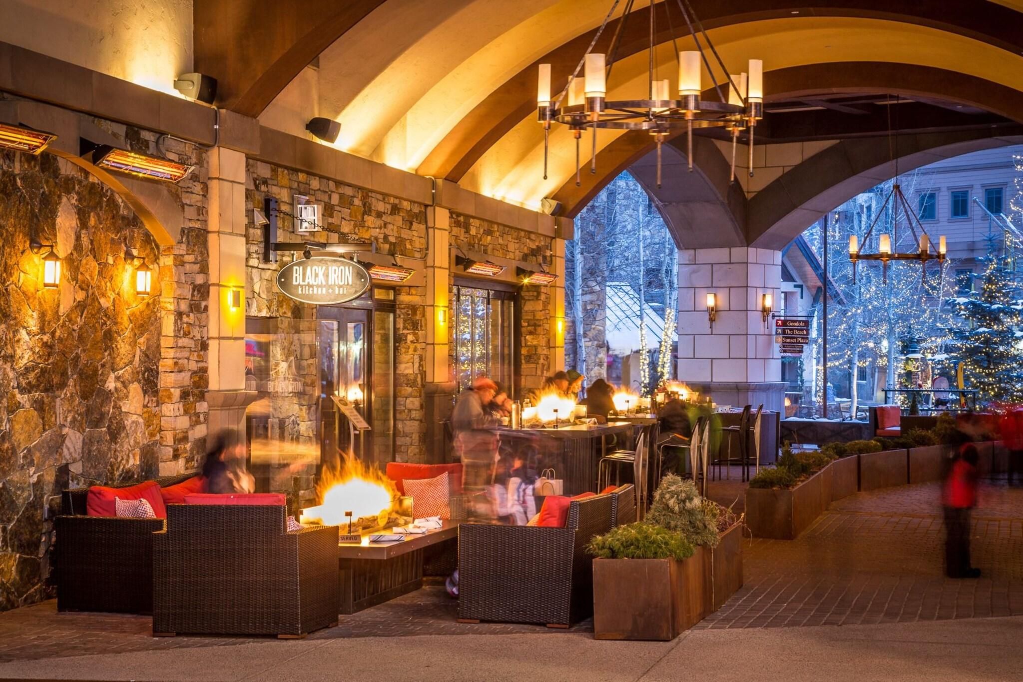 An outdoor dining area with stone walls, wicker furniture, and a fire feature.