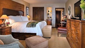 A hotel room with a large bed, a wooden headboard, a dresser, a television, and a desk with a chair.