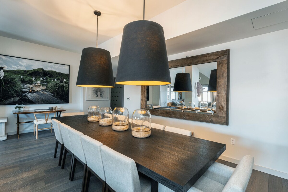 A modern dining area with a dark wooden table, white upholstered chairs, and black pendant lights.