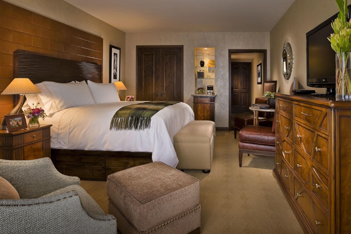A hotel room with a large bed, a dresser, a television, and a desk with a chair.