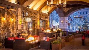 An outdoor dining area with stone walls, wicker furniture, and a fire feature. - Madeline Hotel And Residences, Auberge Resorts (Telluride)