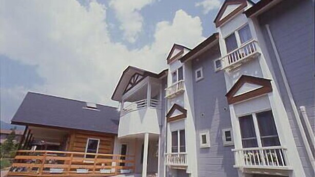A multi-story residential building with balconies, a wooden deck, and a sloped roof. - Petit Hotel C Est Bon (Nikko)