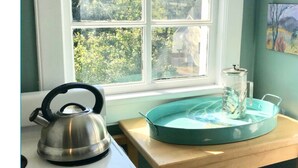 A kitchen with a stove, kettle, and a coffee maker on a wooden table near a window. - Sunny Blue Bungalow near Nashville in Historic Downtown Murfreesboro (Murfreesboro)