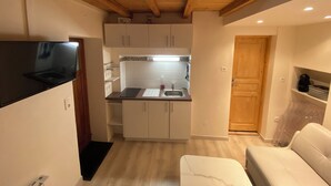 Une cuisine de taille réduite avec des meubles blancs, un plan de travail noir et un plafond en bois.