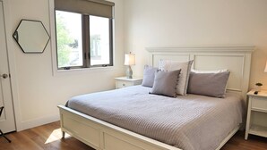 A bedroom with a bed, a nightstand, a lamp, a window, and a door.