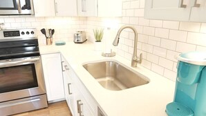 A modern kitchen with stainless steel appliances, a double sink, and a teal coffee maker.