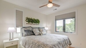 A bedroom with a bed, nightstands, a ceiling fan, a window with blinds, and a wall-mounted plant. - Capri TC: Charming Downtown TC Oasis (Traverse City)