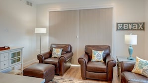 A living room with two brown leather armchairs, a small ottoman, a floor lamp, and a 'Relax' sign on the wall. - Capri TC: Charming Downtown TC Oasis (Traverse City)