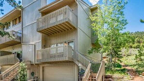 Un immeuble résidentiel à plusieurs étages, doté de balcons, d’un garage et s’intégrant dans un paysage naturel en arrière-plan.