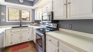 Une cuisine avec des meubles blancs, une cuisinière noire, un four à micro-ondes et une horloge au mur.