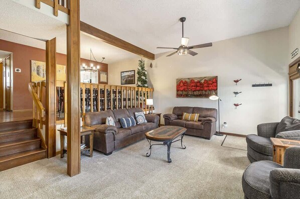 A spacious living room with a brown leather sofa, a wooden coffee table, and a ceiling fan.