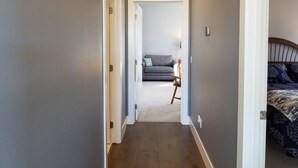 Un pasillo que conduce a un dormitorio con una cama, una mesita de noche y una lámpara.