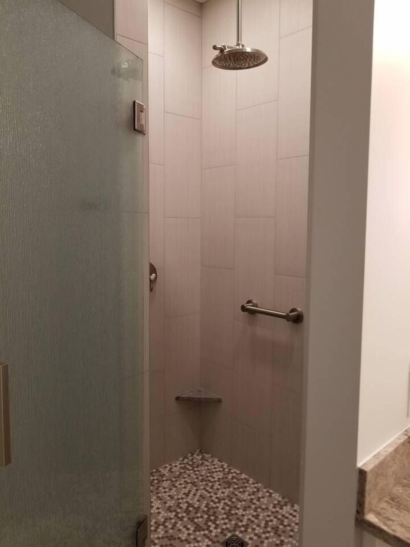 Un espace douche étroit doté d’un pommeau de douche à main, d’une porte en verre et d’un sol carrelé.
