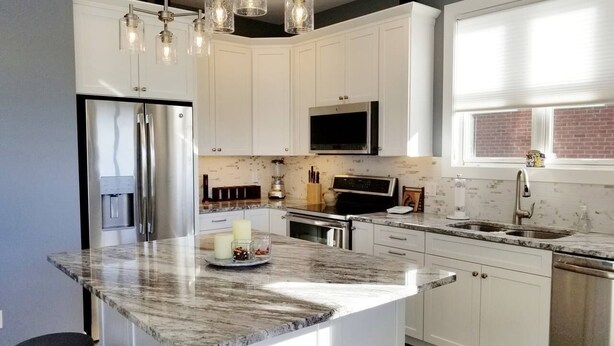 Una cocina moderna con armarios blancos, electrodomésticos de acero inoxidable, una isla de mármol e iluminación colgante.