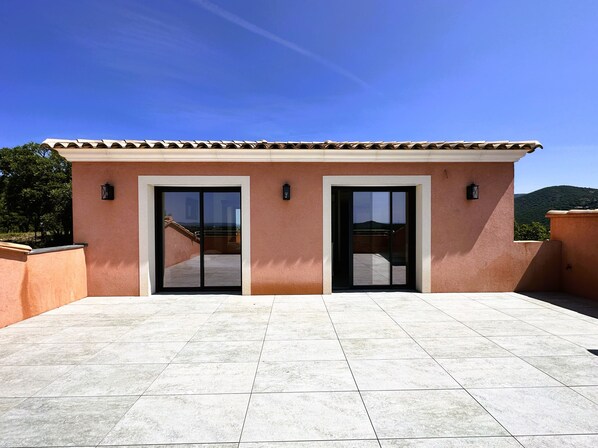 Un edificio con patio empedrado, dos puertas de vidrio correderas y vistas a un paisaje montañoso.