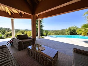 A covered outdoor area with a pool, wicker furniture, and a view of the hills.