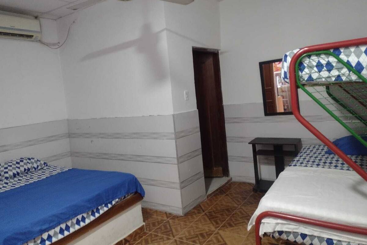 A dormitory room with two bunk beds, a ceiling fan, a small table, and a window with a mirror.