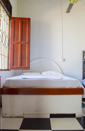 A bed with a wooden headboard and a metal frame, a window with metal bars, and a ceiling fan. - Hostal Maranatha - Hostel (Santa Marta)