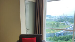 Una habitación con un sofá marrón oscuro, un cojín rojo y vistas a una autopista y zonas verdes al exterior.