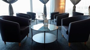 Un salón moderno con una mesa redonda de vidrio, sillones de cuero negro y vistas de la ciudad a través de amplias ventanas.